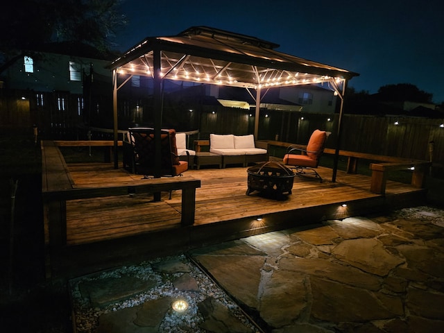 deck at night featuring a gazebo and an outdoor living space with a fire pit