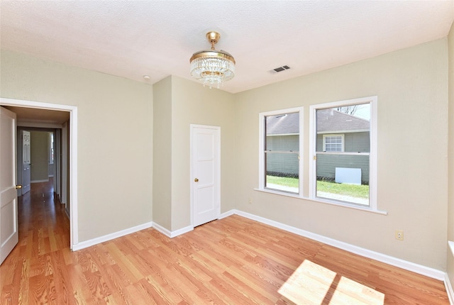 spare room featuring baseboards, visible vents, a chandelier, and light wood-type flooring