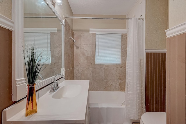 bathroom featuring vanity, toilet, shower / bath combo with shower curtain, and a textured wall