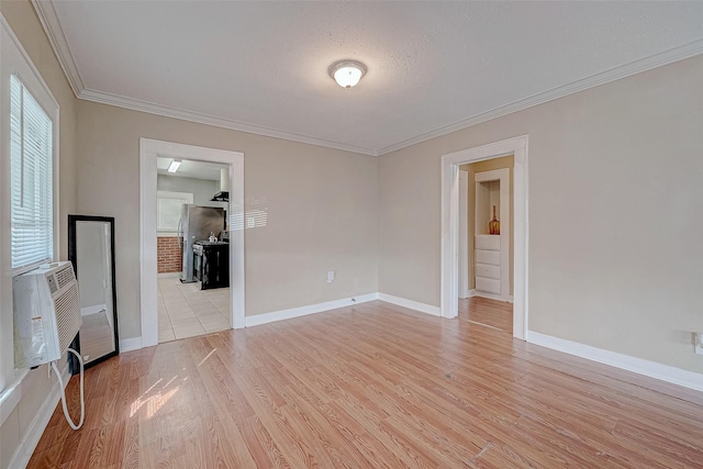 empty room featuring cooling unit, baseboards, light wood-style flooring, and crown molding