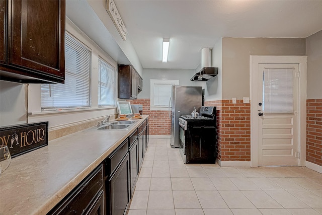 kitchen featuring stainless steel range with gas stovetop, brick wall, wall chimney range hood, and a sink