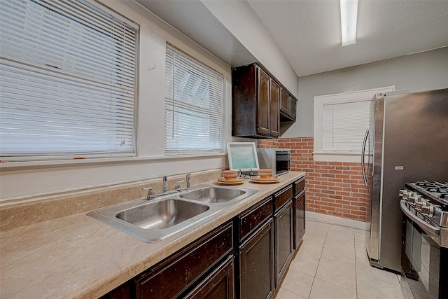 kitchen featuring a sink, stainless steel range with gas cooktop, light countertops, light tile patterned floors, and dark brown cabinets