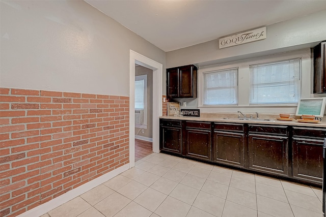 kitchen featuring a sink, brick wall, light tile patterned flooring, and light countertops