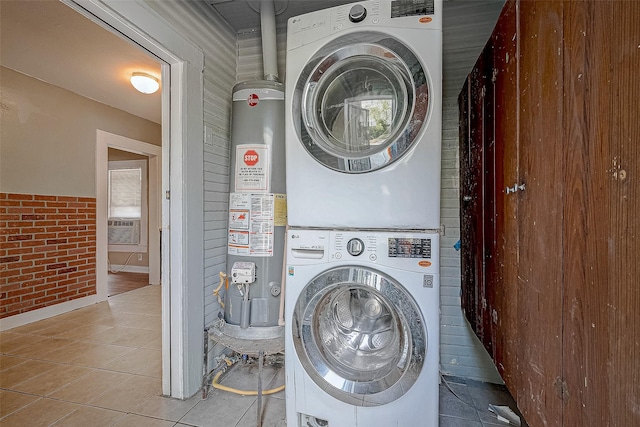 washroom with stacked washer and clothes dryer, water heater, brick wall, tile patterned flooring, and laundry area