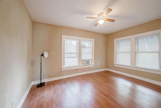 empty room featuring ceiling fan, baseboards, cooling unit, wood finished floors, and a textured ceiling