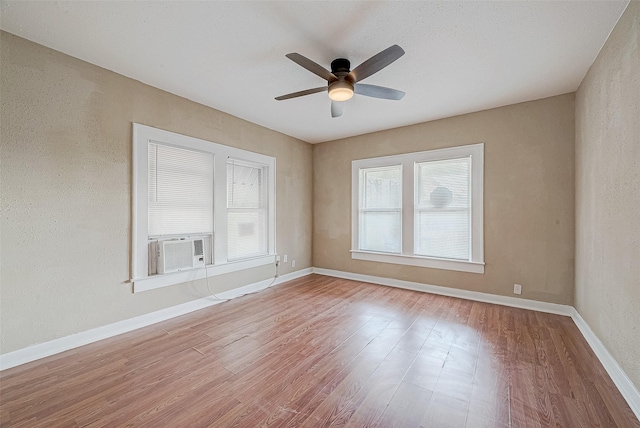 empty room with baseboards, wood finished floors, a ceiling fan, and a textured wall