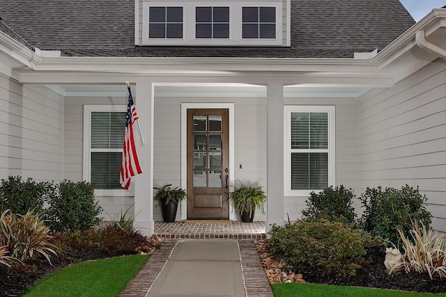 view of exterior entry featuring a porch and roof with shingles