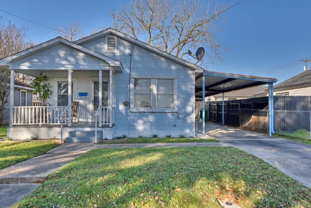 bungalow featuring a porch, fence, concrete driveway, a front yard, and a carport