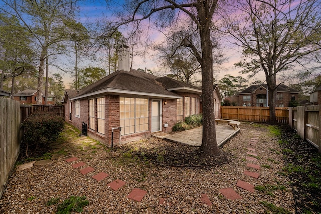 back of property with a patio, brick siding, a fenced backyard, and a chimney