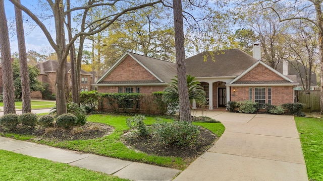 view of front of property featuring brick siding, a front lawn, concrete driveway, roof with shingles, and a chimney