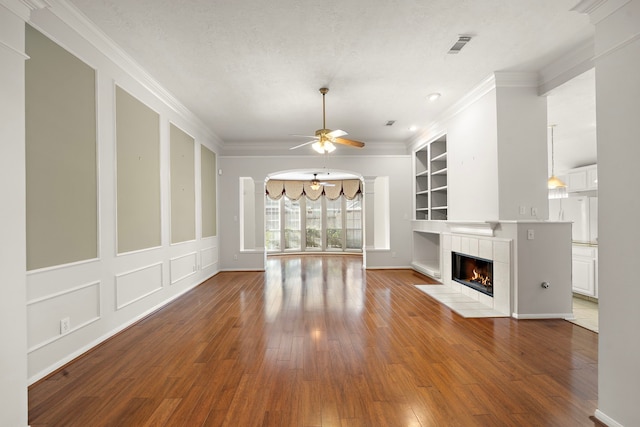 unfurnished living room with a fireplace, built in features, ceiling fan with notable chandelier, and ornamental molding