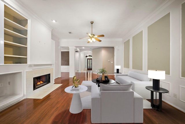 living area featuring built in shelves, wood finished floors, a fireplace, ceiling fan, and crown molding