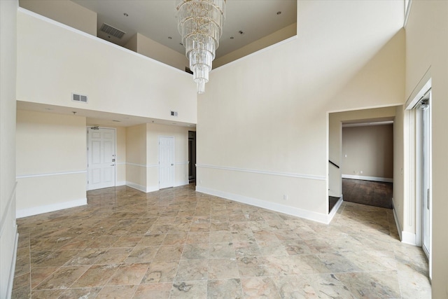 spare room featuring visible vents, baseboards, an inviting chandelier, and a towering ceiling