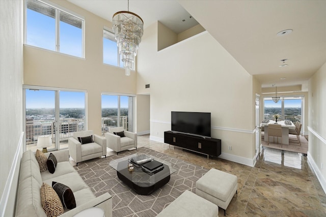 living room featuring an inviting chandelier, stone finish floor, baseboards, and a towering ceiling