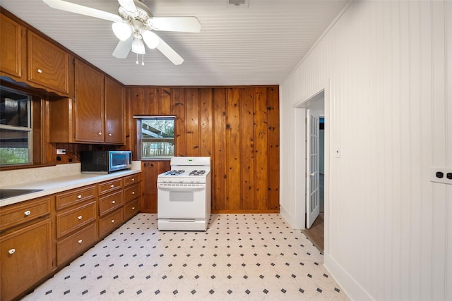 kitchen with brown cabinets, stainless steel microwave, light countertops, light floors, and white gas range