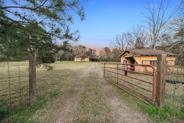 view of road featuring a rural view, driveway, a gated entry, and an exterior structure