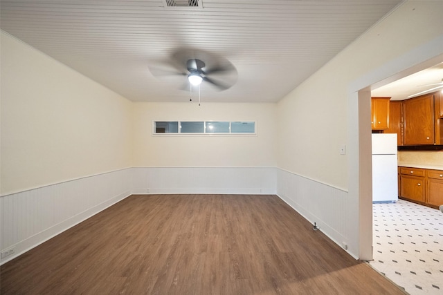 spare room with a wainscoted wall, visible vents, ceiling fan, and wood finished floors