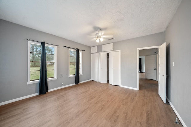 unfurnished bedroom featuring light wood-type flooring, a textured ceiling, a closet, baseboards, and ceiling fan