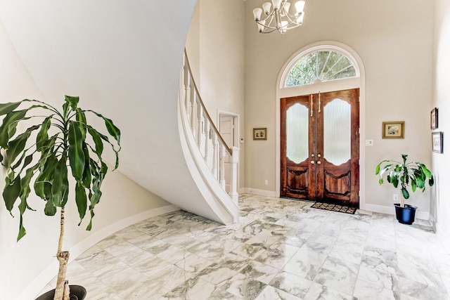 foyer entrance with a towering ceiling, baseboards, a chandelier, and stairs