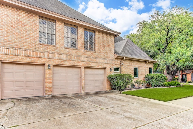 view of front facade with a front lawn, brick siding, driveway, and a shingled roof