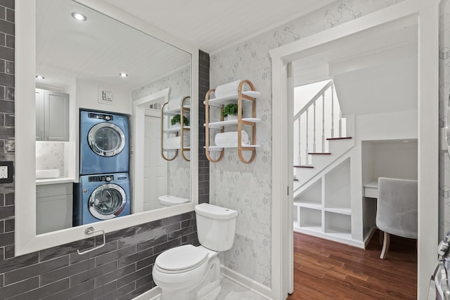 bathroom with wallpapered walls, toilet, recessed lighting, stacked washer and clothes dryer, and wood finished floors