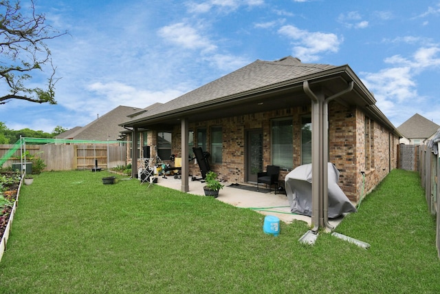 rear view of property featuring a fenced backyard, a shingled roof, a lawn, a patio area, and brick siding