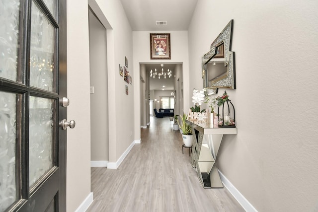 hallway featuring visible vents, baseboards, and light wood finished floors