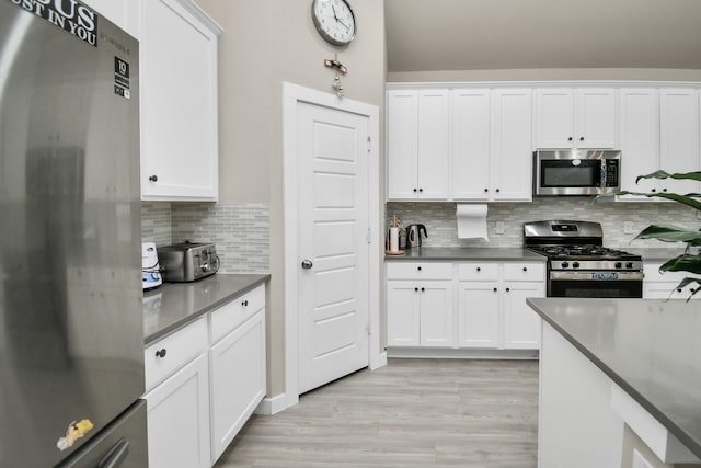 kitchen featuring backsplash, dark countertops, stainless steel appliances, light wood-style floors, and white cabinets