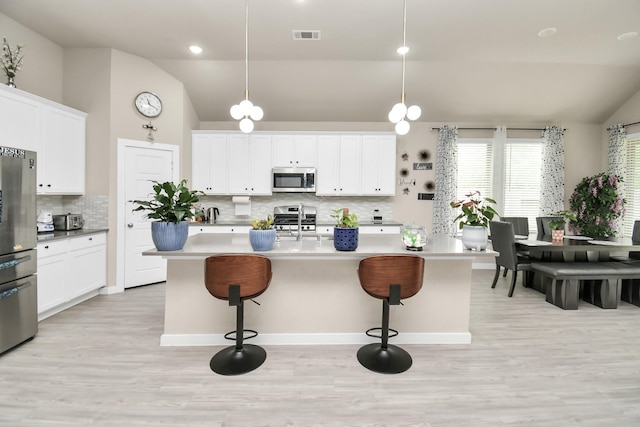 kitchen featuring stainless steel appliances, visible vents, a breakfast bar area, and vaulted ceiling