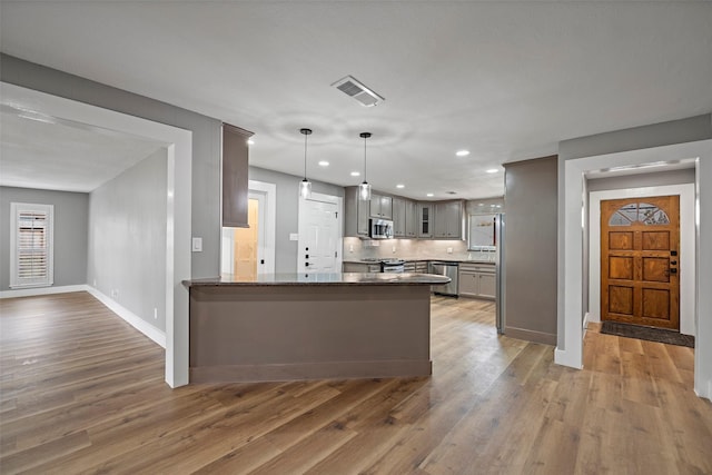 kitchen with visible vents, appliances with stainless steel finishes, a peninsula, light wood finished floors, and glass insert cabinets