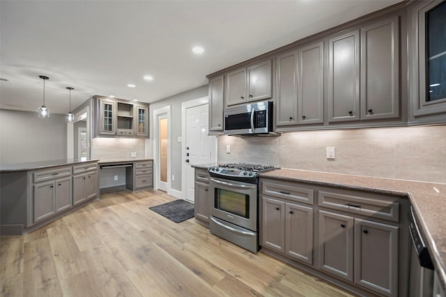 kitchen with backsplash, glass insert cabinets, decorative light fixtures, light wood-style flooring, and stainless steel appliances