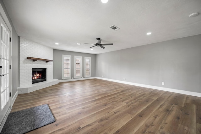 unfurnished living room with visible vents, a fireplace, baseboards, and wood finished floors