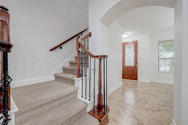 entrance foyer featuring arched walkways, stairway, baseboards, and ornamental molding