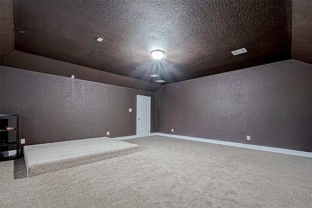 carpeted spare room featuring vaulted ceiling, a textured wall, visible vents, and a textured ceiling