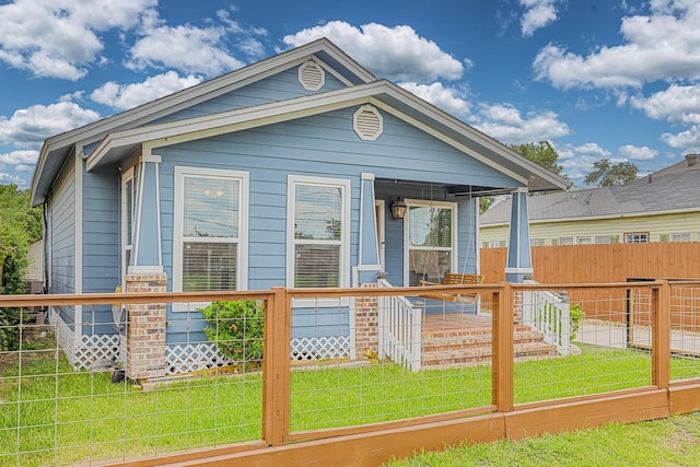 shotgun-style home featuring covered porch, a front yard, and fence