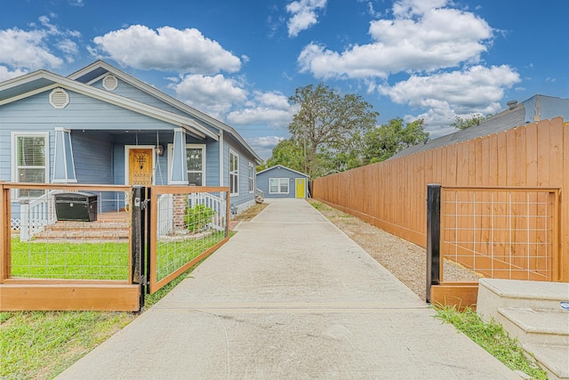 exterior space with driveway, a gate, a fenced front yard, a porch, and an outdoor structure