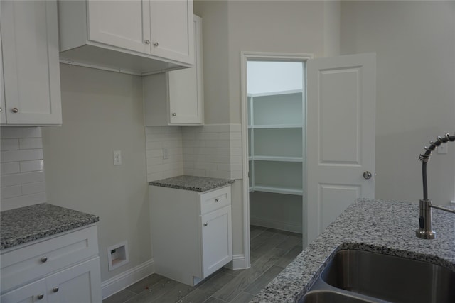 kitchen featuring white cabinets, light stone counters, and a sink