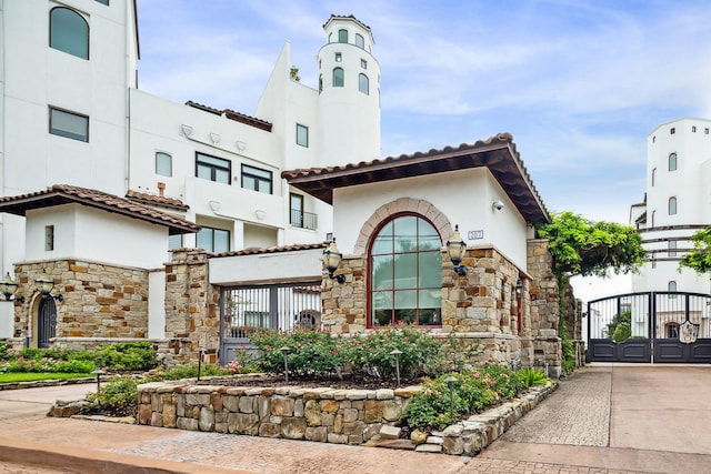 mediterranean / spanish-style house featuring a gate, stone siding, and stucco siding