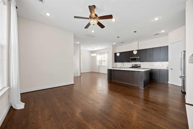 kitchen with dark wood finished floors, open floor plan, a center island with sink, light countertops, and stainless steel appliances