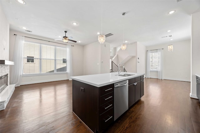 kitchen with dark wood-style flooring, a sink, a stone fireplace, light countertops, and stainless steel dishwasher