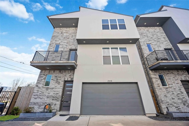 contemporary house featuring stucco siding, a balcony, fence, concrete driveway, and brick siding