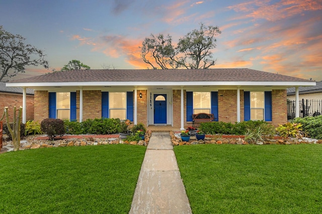 ranch-style home featuring a porch, fence, a lawn, and brick siding