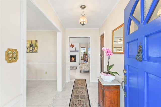 foyer entrance with marble finish floor, a warm lit fireplace, baseboards, and ornamental molding