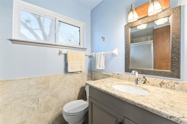 bathroom with a shower stall, tile walls, toilet, wainscoting, and vanity