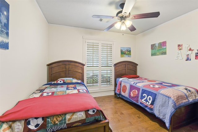 bedroom with a ceiling fan, wood finished floors, visible vents, and ornamental molding