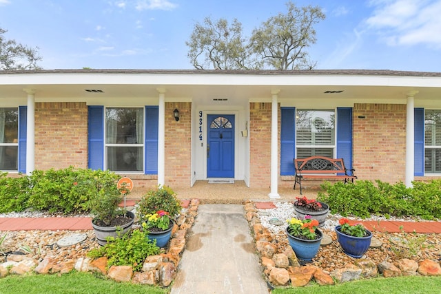 entrance to property with a porch and brick siding