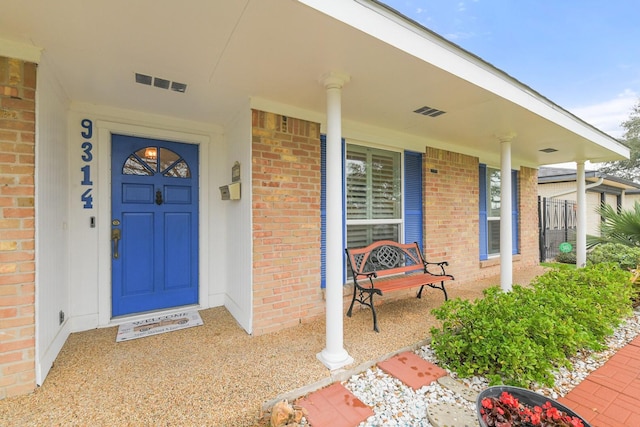 entrance to property with visible vents, brick siding, and a porch