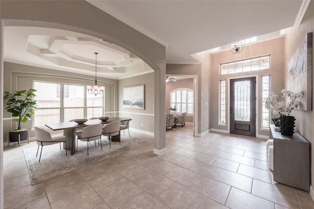 foyer with baseboards, a tray ceiling, ornamental molding, light tile patterned floors, and arched walkways