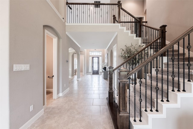 foyer entrance with baseboards, arched walkways, a high ceiling, and stairs