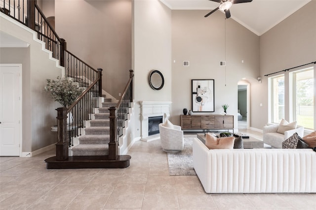 living area with baseboards, ornamental molding, arched walkways, a glass covered fireplace, and a ceiling fan